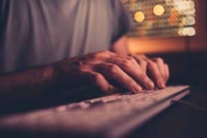 Start a Business Podcast: Gear, Editing and Leads 4 Hands typing on a keyboard illuminated by soft, warm lighting, emphasizing digital marketing and SEO services offered by Wapiti Digital.